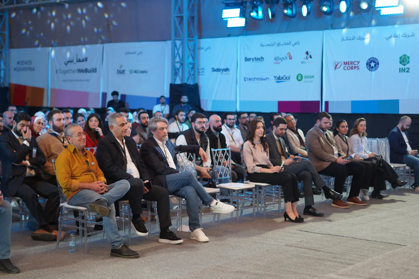 The GEW Syria audience seated in front of partner banners reading Together We Build