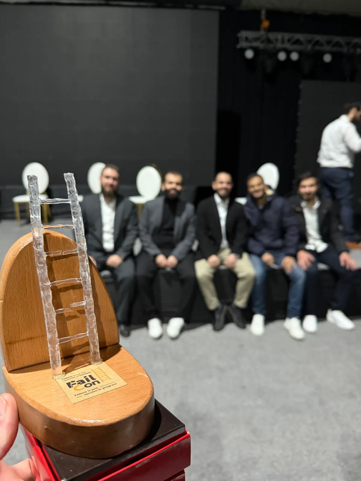 The FailCon keepsake, a glass ladder on a wooden base, held up in front of the speakers