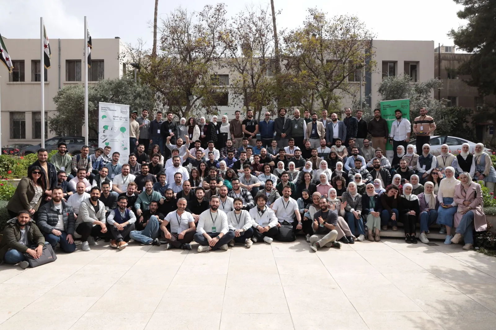 The Startup Weekend Syria cohort outdoors beside a banner reading Techstars Startup Weekend Syria, April 16 to 18